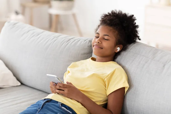 Afrikaans meisje genieten van muziek online dragen oordopjes ontspannen thuis — Stockfoto