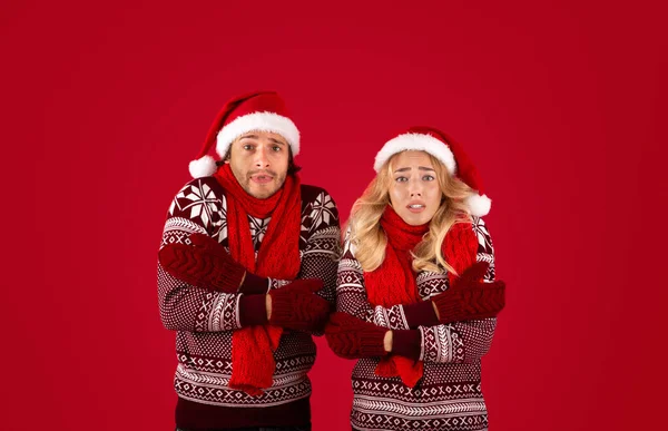 Різдвяний охолоджувач. Молода пара в зимовому вбранні тремтить на червоному тлі — стокове фото