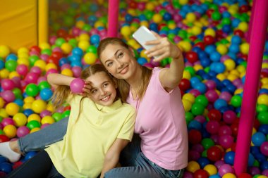 Anne ve kızı çocukların oyun merkezinde top havuzunda selfie çekiyorlar.