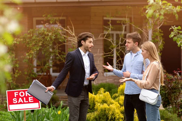 Corredor de bienes raíces discutiendo con clientes molestos frente a la casa de campo al aire libre —  Fotos de Stock