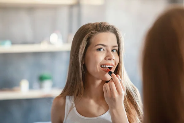 Beauty and makeup. Pretty lady applying lipstick near mirror indoors — Stock Photo, Image