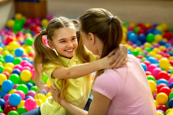 Glada flicka kramar sin mamma i bollen grop på inomhus barn lekplats — Stockfoto