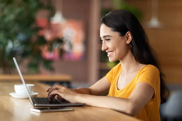 Glada flicka frilansare skriva på laptop tangentbord, café interiör — Stockfoto