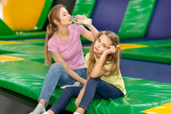 Yorgun kız ve genç anne trambolinde su içiyor.