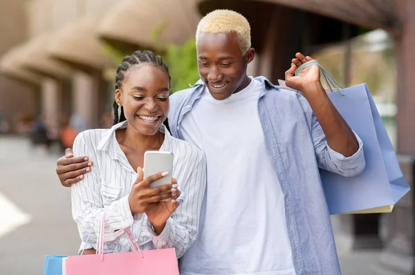 Birçok renkli paketi olan neşeli Afro-Amerikan çifti akıllı telefona bakar ve yeni bir alışveriş yapar.