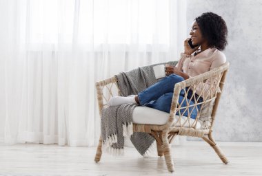 Koltukta dinlenen, çay içen ve cep telefonuyla konuşan mutlu siyah kadın.