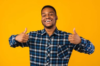 Siyah adam başparmaklarını iki eliyle havaya kaldırıyor, sarı arka plan
