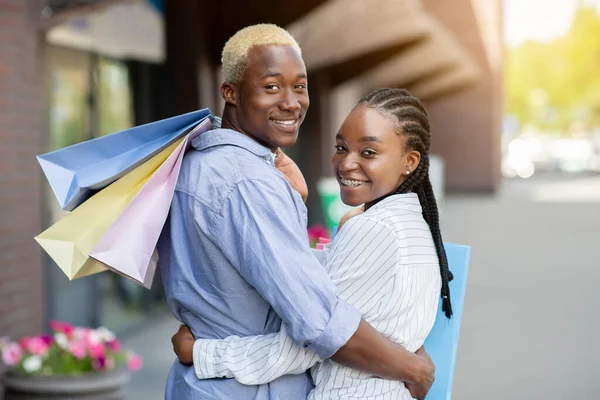 Détente après les courses. Couple afro-américain souriant avec des sacs colorés marchant à la maison après la boutique — Photo