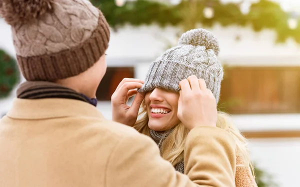 Guy pokrývající přítelkyně oči s kloboukem, zatímco baví venku spolu v zimě — Stock fotografie