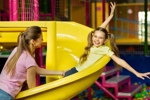 Family recreation. Cute girl with her mom on slide at indoor children playground