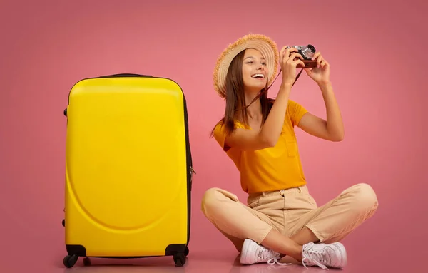 Glückliches Mädchen, das Fotos vor der Kamera macht und neben dem Gepäck sitzt — Stockfoto