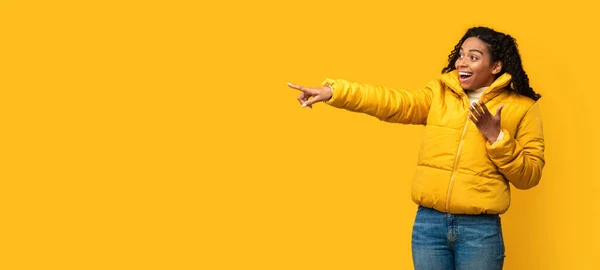 Aufgeregtes Mädchen in Jacke, Finger zur Seite zeigend, gelber Hintergrund, Panorama — Stockfoto