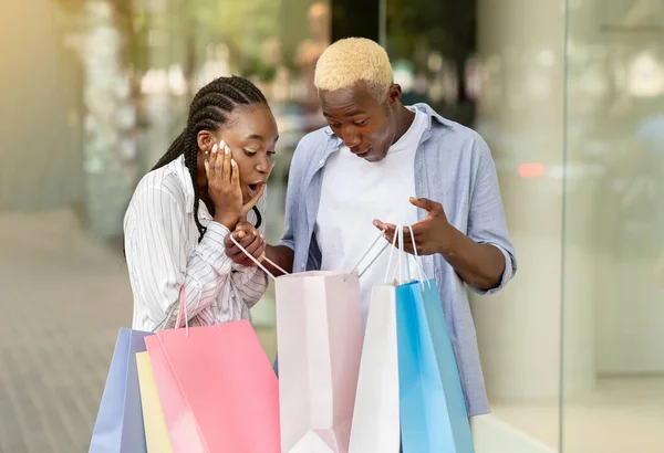 Drukt emoties geluk Afrikaanse Amerikaanse man tonen aankopen in boodschappentas naar meisje in de buurt van etalage — Stockfoto