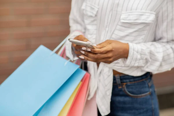 Mensaje sobre venta, bono o reembolso. Chica afroamericana con bolsas de compras con compras, escribiendo por teléfono — Foto de Stock