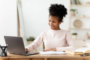 Afrikalı kız ev ödevini laptopta yapıyor. İnternette çalışıyor.