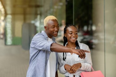 Harika, mükemmel indirimler. Mutlu Afrikalı Amerikalı adam alışveriş merkezinin vitrinini işaret ediyor.