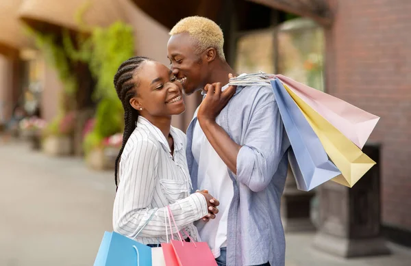 Liefde, vrije tijd en winkelen. Vrolijk Afrikaans amerikaanse jongen kust meisje met gekleurde zakken — Stockfoto