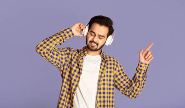 Kulaklıklı havalı Hintli adam leylak arka planda en sevdiği müziğin keyfini çıkarıyor.