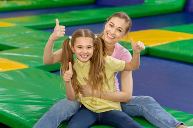 Eğlenceli aile aktiviteleri. Anne ve kızı kapalı trambolin parkında baş parmağını kaldırıyor.