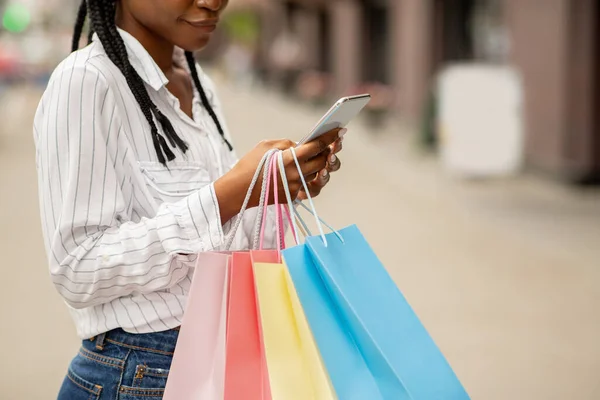 ショッピングのための近代的な技術。アフリカ系アメリカ人の女の子のブロガーはバッグを保持し、スマートフォンで入力 — ストック写真