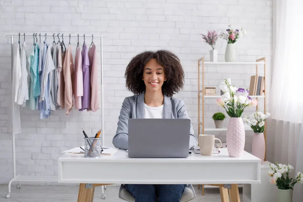 Casa de diseño de ropa, diseñador de moda trabajando. Chica afroamericana feliz mirando el ordenador portátil — Foto de Stock