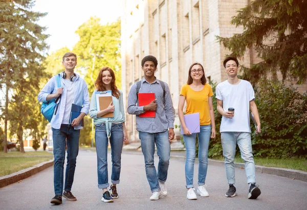 Groep studenten lopen glimlachend naar camera in de buurt van het universiteitsgebouw — Stockfoto