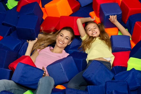 Por encima de la vista de mamá feliz con su hija acostada entre cubos suaves en el parque de atracciones para niños — Foto de Stock