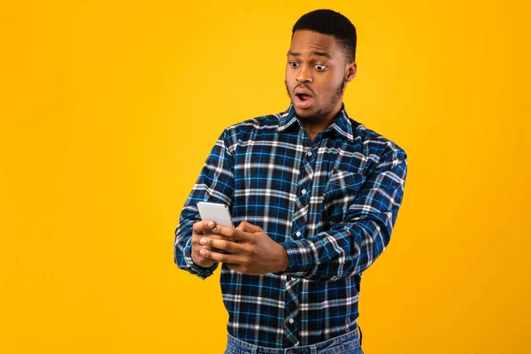 Homem africano segurando celular leitura Wow notícias sobre fundo amarelo — Fotografia de Stock