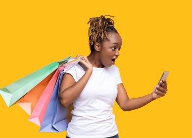 Alışveriş torbalarıyla telefon ekranına bakan afrikalı bir kız.