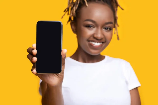 Menina preta alegre mostrando smartphone com tela em branco — Fotografia de Stock