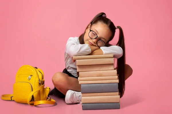 Conceito triste e cansado. Menina de óculos de uniforme com mochila dorme na pilha de livros — Fotografia de Stock