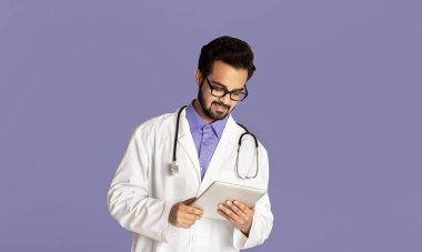 Çevrimiçi doktor danışmanlığı. Tablet bilgisayarlı yakışıklı Hintli sıhhiyeci leylak arkaplanı üzerinden internet üzerinden istemciyle konuşuyor