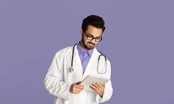 Läkarkonsultation online. Snygg indisk läkare med surfplatta dator talar med klienten på webben över lila bakgrund — Stockfoto