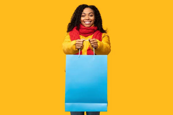 Щаслива чорна жінка показує велику сумку для покупок на жовтому тлі — стокове фото