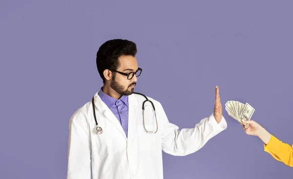 Зменшення хабарництва та корупції. Чесний індійський лікар відмовляється брати гроші у пацієнта на фіолетовому фоні — стокове фото