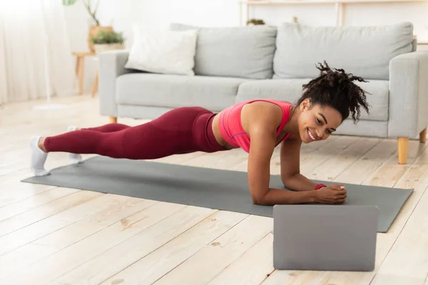 Schwarze Frau macht Plank-Übung am Laptop während des Trainings in Innenräumen — Stockfoto