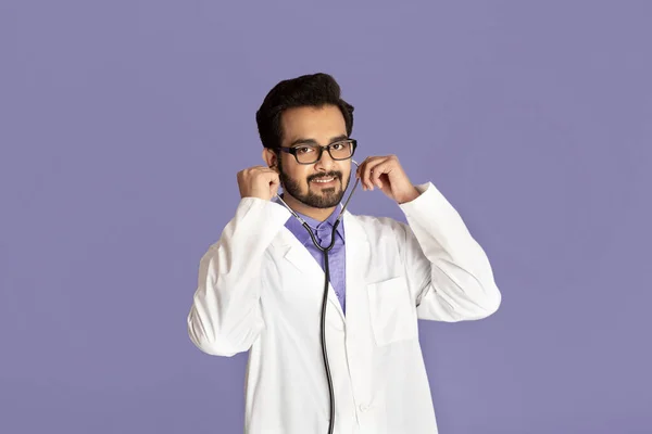 Retrato del alegre médico indio en bata de laboratorio con estetoscopio sobre fondo violeta — Foto de Stock