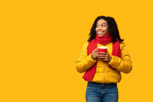 Μαύρο κορίτσι φορώντας χειμωνιάτικο σακάκι που κρατά την κούπα του καφέ, κίτρινο φόντο — Φωτογραφία Αρχείου