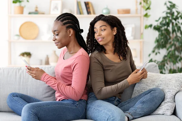 Jovens negras sentadas de costas para trás, usando smartphones — Fotografia de Stock