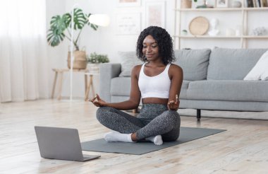 Huzurlu siyahi kadın evde laptopun önünde meditasyon yapıyor.