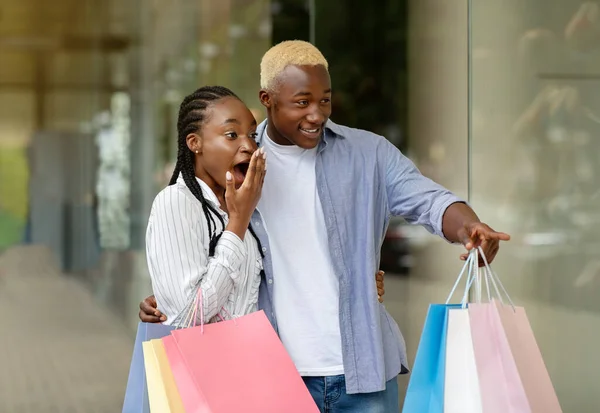 Quero-o agora. Jovem afro-americano chocado aponta para vitrine, para menina — Fotografia de Stock