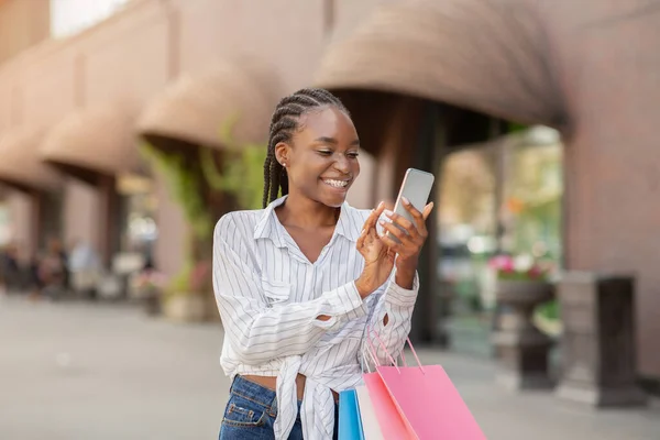 Portrait of woman holding packages and smartphone, shocked by online fashion store