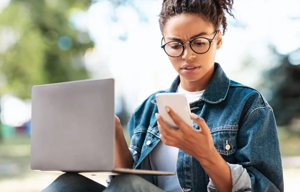 Mujer negra leyendo mensaje en el teléfono frunciendo el ceño trabajando al aire libre — Foto de Stock