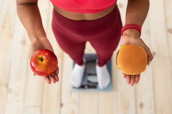 Dziewczyna wybierająca między hamburgerem a jabłkiem stojącym na wadze — Zdjęcie stockowe