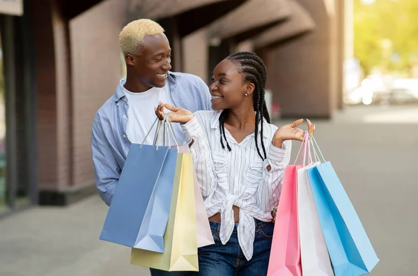 Vente saisonnière. Couple afro-américain souriant avec des sacs colorés se regardant — Photo