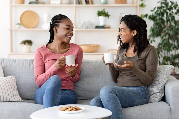 Afrikanska amerikanska flickvänner njuter av helgen tillsammans, dricker kaffe på soffan — Stockfoto