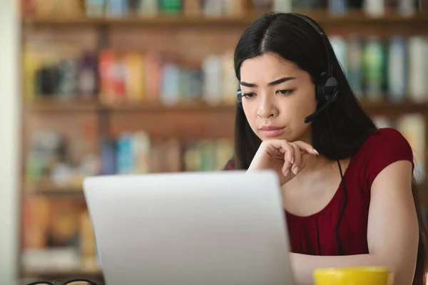 Jovem asiática feminina usando laptop e fone de ouvido, trabalhando online no interior do café — Fotografia de Stock