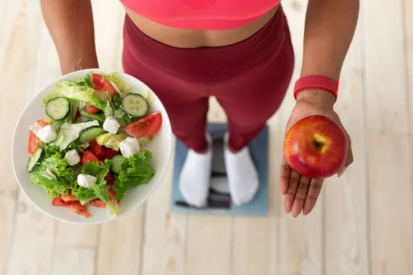 Frau steht auf Waage und hält Salat und Apfel drinnen, beschnitten — Stockfoto