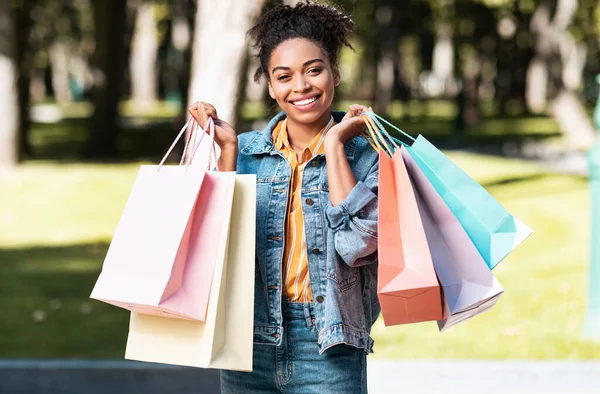 Chica africana feliz sosteniendo coloridas bolsas de compras de pie al aire libre — Foto de Stock