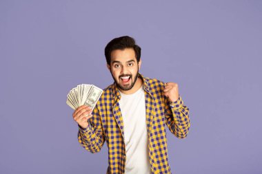 Büyük kazanç konsepti. Heyecanlı Hintli adam para hayranı menekşe arka planında EVET işareti yapıyor
